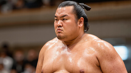 close-up of a sumo wrestler standing in the ring with a determined expression, body glistening under the lights before competition begins
