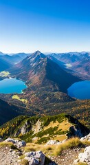 A scenic high-angle view of a mountain range. Two alpine lakes appear between the verdant peaks, under a bright blue sky