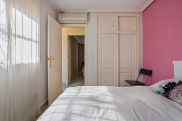 Sunlit pink-accented bedroom with built-in wardrobe and soft white furnishings
