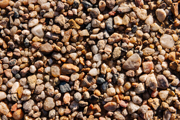Colorful river pebbles in warm sunlight, close up macro texture of rounded stones and quartz fragments, natural gravel background for design and construction concepts.