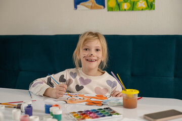 Girl drawing cute illustration with paints in children's room.