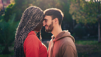 Romantic interracial couple touching foreheads during an intimate moment at golden hour sunset, showing love, tenderness, emotional connection and authentic affection outdoors