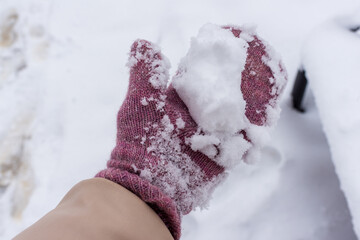 A pink knitted glove holds a handful of fluffy snow, capturing a playful winter moment. The close-up highlights soft textures, cold-season mood, and cozy holiday feeling associated with outdoor winter