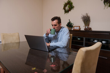 Man Working From Home: Coffee Sip at Laptop in Festive Dining Room