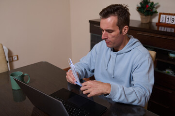 Home Office Moment: Busy Dad Working Remotely, Reviewing Documents With Laptop