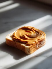 Slice of bread on a white rectangular plate. the bread appears to be toasted and has a golden brown crust. on top of the bread, there is a generous amount of peanut butter spread in a swirl pattern.