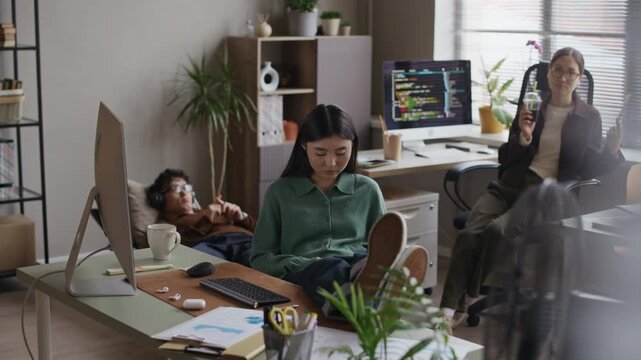 Long shot of three young Asian startup coworkers having break in modern office workspace