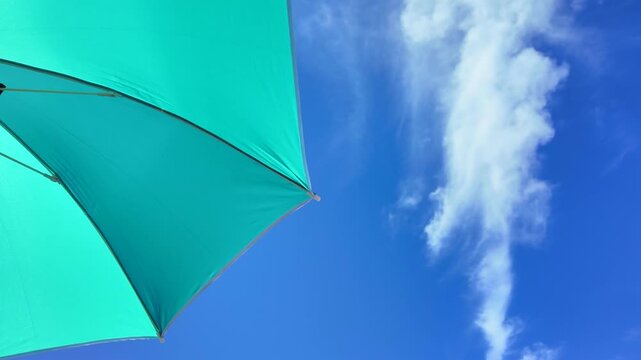 Beach umbrella swaying in the wind against a bright blue sky, evoking peace, relaxation and vacation vibes.