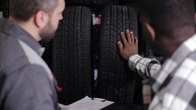 African young adult male choosing tires with salesperson caucasian men in store.