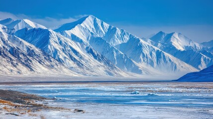 Majestic snow-capped mountain range dominates a frozen valley landscape under a clear blue sky