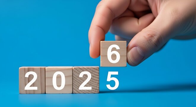 Hand placing a wooden block with the number six to complete the year 2026 on a blue background
