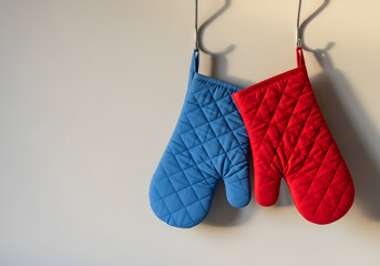 Red and blue quilted oven mitts hanging on hooks against wall  