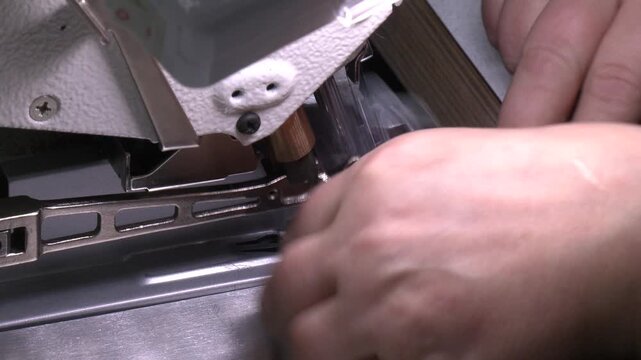 The main working segment of the overlock is a foot with two needles. Fingers hand of seamstress with needle presser foot and thread of industrial sewing machine to sew seam of black cloth close-up
