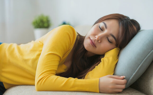 A young asian woman sleeping peacefully on a couch, resting her head on a pillow, conveying relaxation, comfort, and a moment of quiet repose - Powered by Adobe