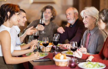 Multi-generation family discussing daily life while having fresh food and wine in restaurant