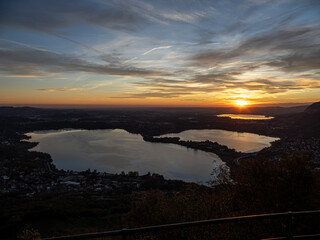 A breathtaking aerial view of the sunset over the two Brianza lakes (Annone and Pusiano) in Lombardy, Italy, with mountains silhouetted on the horizon. 