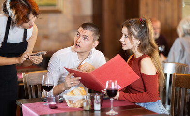 Young woman waitress takes order from couple young man and young woman in restaurant