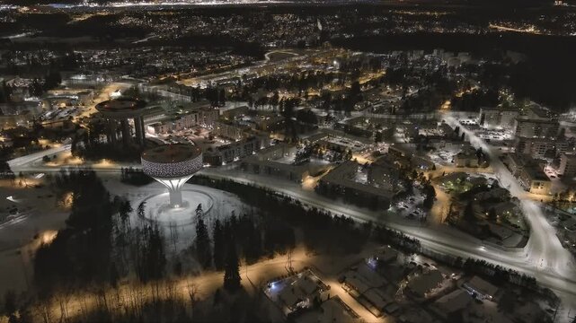 Vantaa.Finland-December 29.2021: Drone shot of the new Hiekkaharju water tower next to the old one in Vantaa. Wintertime. Nighttime. Awesome cityscape. Camera slowly tilting downwards.