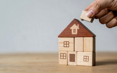 Hand building a house with wooden blocks, symbolizing home construction, real estate investment, and family security, with a focus on the final piece being placed