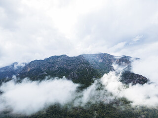 Aerial drone photo of mountains covered in green forest and surrounded by clouds. Dramatic atmosphere with natural light and mist