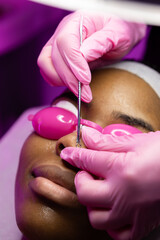 Fototapeta premium African woman in beauty clinic doing a facial evaluation and a cosmetology treatment. Woman on an esthetician appointment of facial. use mask do skincare routine