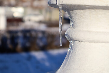 An icicle hanging from a white vase against the backdrop of a winter park