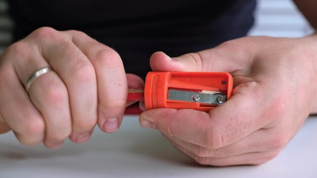 Male hands hold the sharpener and sharp the wooden pencil. The sharpening of construction pencil. Office and art stationery. High quality 4k footage.