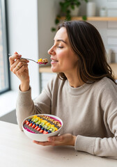 Woman tasting a colorful smoothie bowl while sitting indoors  