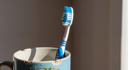 Toothbrush standing in an old mug on a table in natural light  
