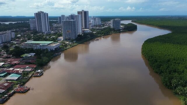 Aerial drone view of a modern city skyline contrasting with a wide, muddy river and lush green mangrove forest