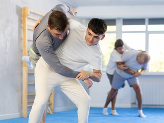 Adult man and young guy training judo techniques in studio..