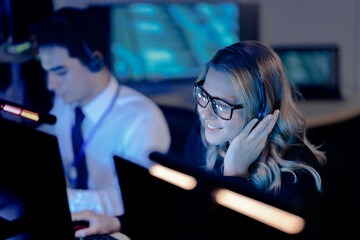 Dynamic night shift collaboration. Male manager provides guidance to a focused male colleague wearing a headset at his computer in a modern tech office during an intense work session.