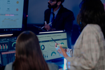 Professional data analysts team collaborating on digital strategy at night. Diverse group examining complex business charts and futuristic dashboard screens in a modern high-tech office environment.