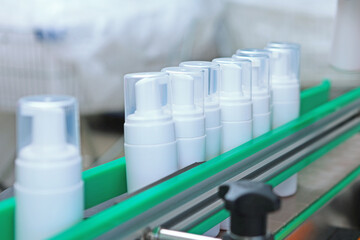 White plastic bottles move along the conveyor belt. Manufacture of cosmetics and skin care products. A capping and labeling machine.