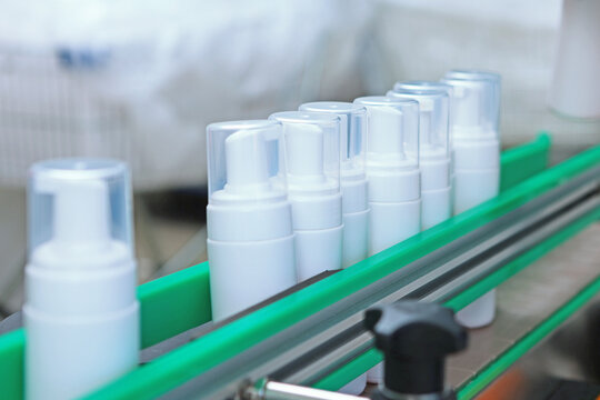 White plastic bottles move along the conveyor belt. Manufacture of cosmetics and skin care products. A capping and labeling machine.