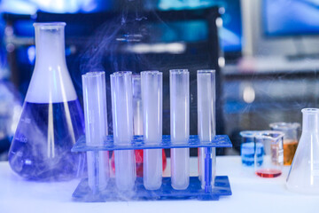 Laboratory glassware including test tubes and flasks emitting cold vapor or smoke in a blue-lit science lab, representing chemical experiments and medical research.