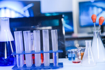 Laboratory glassware including test tubes and flasks emitting cold vapor or smoke in a blue-lit science lab, representing chemical experiments and medical research.
