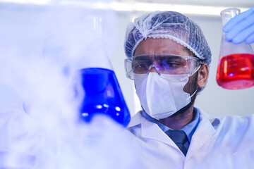 Focused male scientist in protective gear analyzing chemical samples in test tubes within a modern...