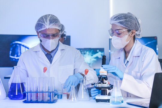 Diverse team of scientists in protective gear collaborating in modern blue lab, analyzing DNA helix structure on monitor and testing chemical samples for medical research.