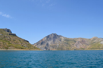 Stunning turquoise water foreground with dry, sun-drenched green mountain background.