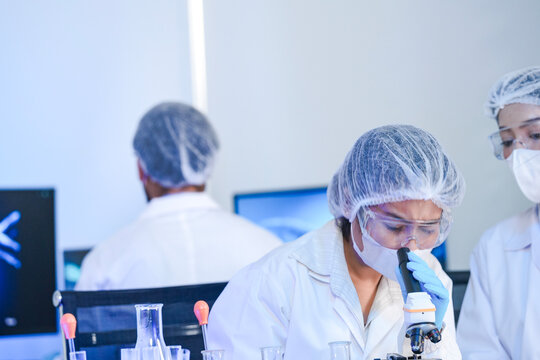 Diverse team of scientists in protective gear collaborating in modern blue lab, analyzing DNA helix structure on monitor and testing chemical samples for medical research.
