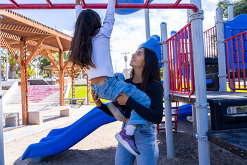 Mother lifting daughter, assisting her on the monkey bars in a park