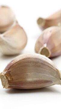Fresh garlic cloves twirling in a close up view on a pristine white backdrop. This flavorful and intense herb is commonly utilized for both culinary purposes and its potential health advantages