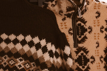 Close-up of two warm brown beige sweaters with unique patterns and textures. Two cozy sweaters hang together, showcasing intricate designs, soft, inviting fabrics for the colder seasons. Fall fashion. © vita
