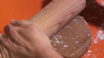 Wooden rolling pin flattening and shaping gingerbread dough on a silicone mat