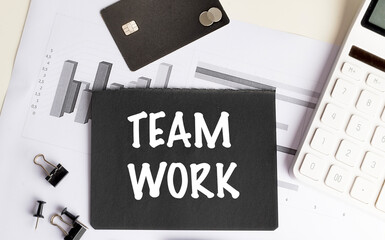 Team work phrase on black paper surrounded by charts, calculator, bank card, and office supplies