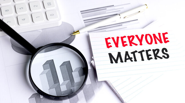 Note with text everyone matters on desk with financial charts, pen, magnifying glass and calculator