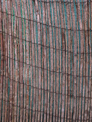 Close-up of a woven natural dry reed or cane screen or matting texture. Canes tied with wire, fence concealment, shading, terrace dividing spaces, rustic material, mediterranean outdoor privacy.