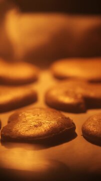 Vertical close-up of gingerbread cookies baking in the oven under warm light