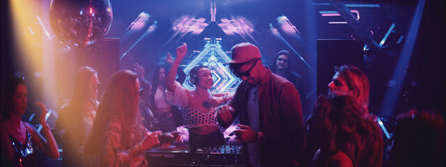 Nightlife scene in a club with DJ and lively crowd enjoying music and dancing under colorful lights